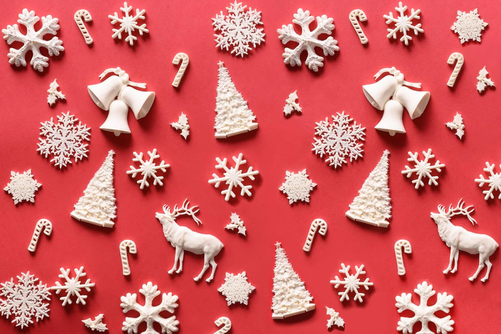 White Christmas trees, bells, snowflakes and reindeer arranged on a festive red background.